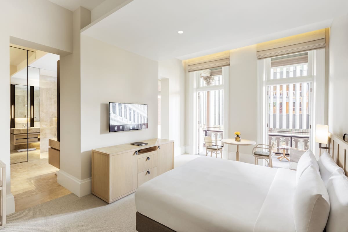Ein Hotelzimmer mit einem großen Bett, einem Schreibtisch, einem Stuhl, einem kleinen Tisch mit einer Lampe und einem Fernseher an der Wand.