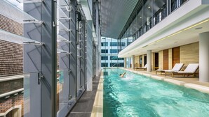 An indoor swimming pool with a person swimming, surrounded by glass walls and modern architecture. - COMO The Treasury (Perth)