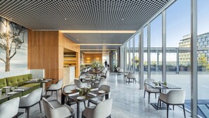 A modern restaurant with a high ceiling, large windows, and a mix of seating arrangements. - COMO The Treasury (Perth)