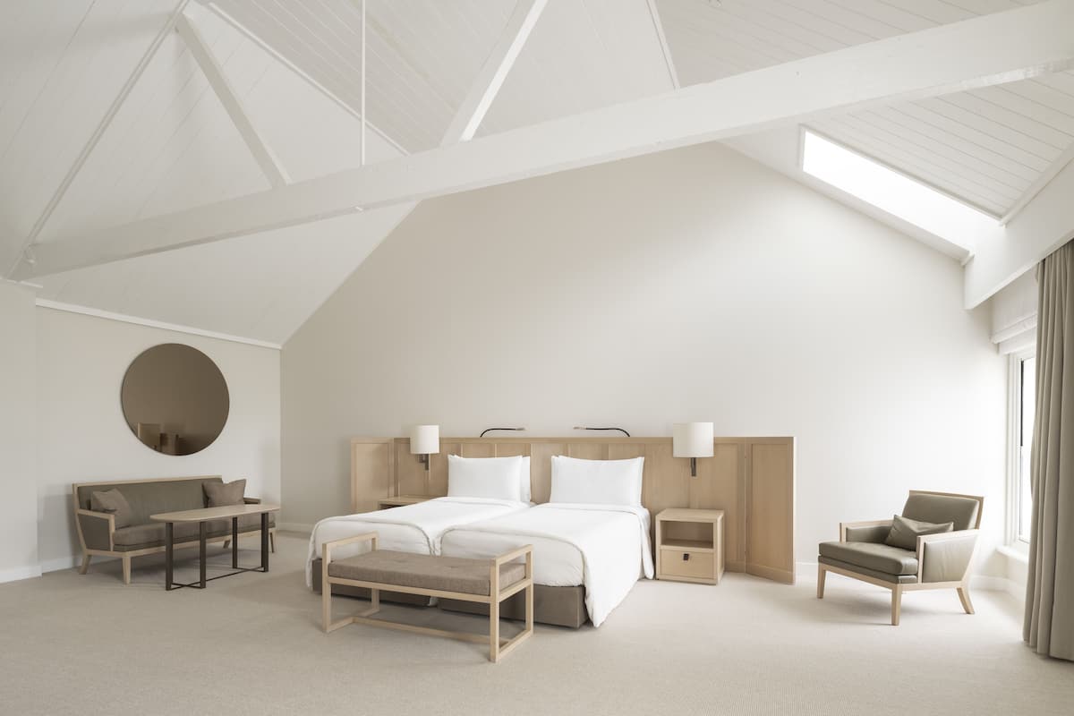 Ein geräumiges, modernes Schlafzimmer mit einem großen Bett, einem Sofa, einem Sessel und einem runden Spiegel.