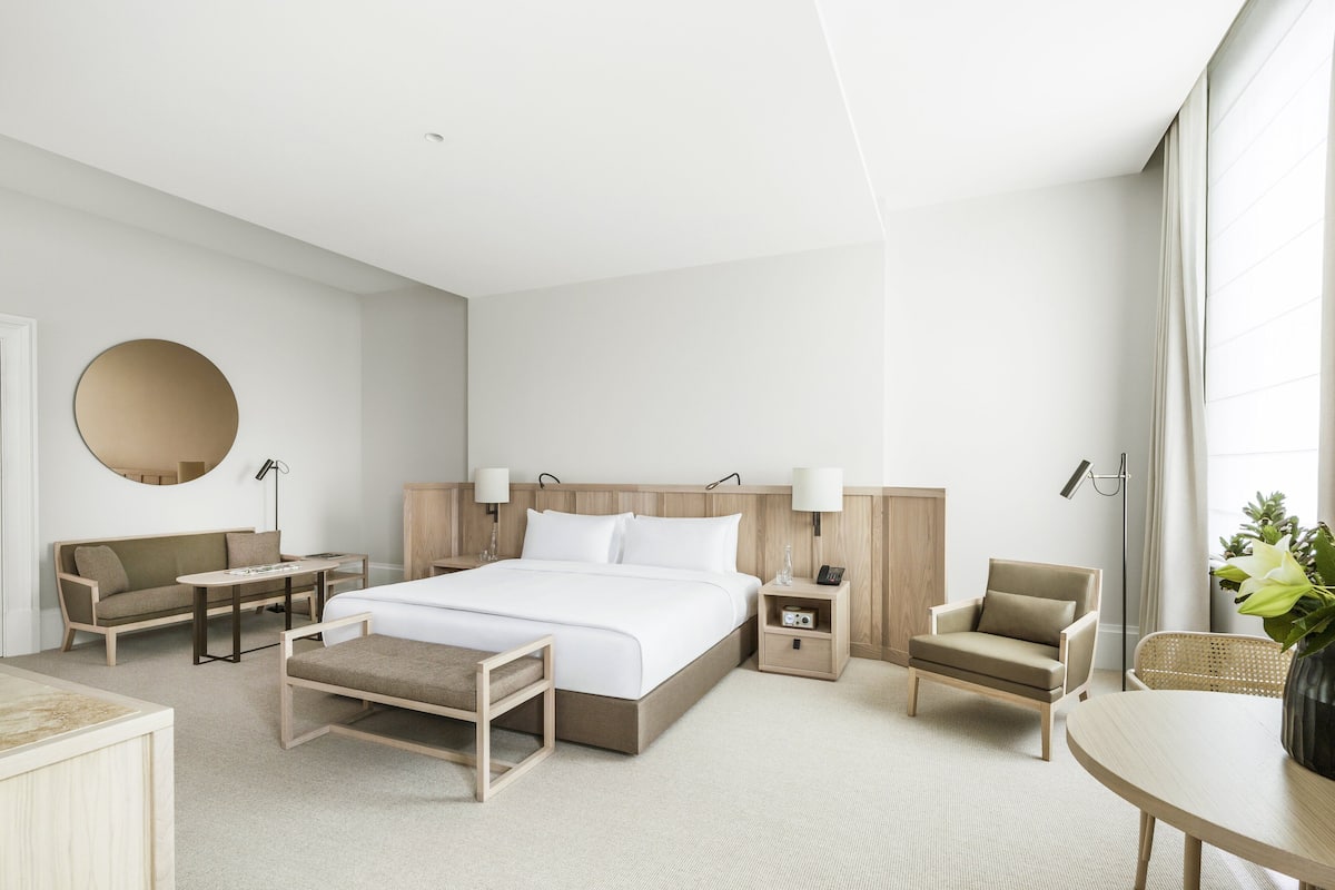 Ein modernes Hotelzimmer mit einem großen Bett, einer Couch, einem Sessel, einem kleinen Tisch und einem Schreibtisch.