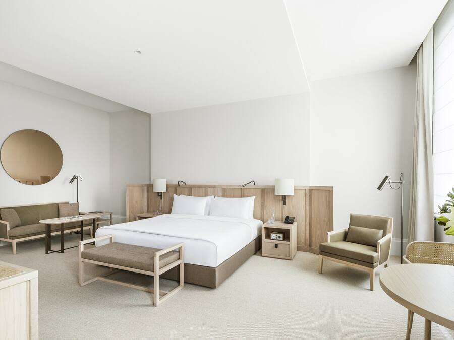 A modern hotel room with a large bed, a sofa, a chair, a small table, and a desk.