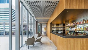 A modern bar area with a wooden counter and shelves of bottles, large windows, and seating. - COMO The Treasury (Perth)