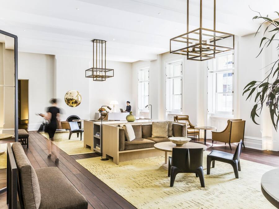 A modern hotel lobby with a sofa, chairs, a round table, and a large plant.