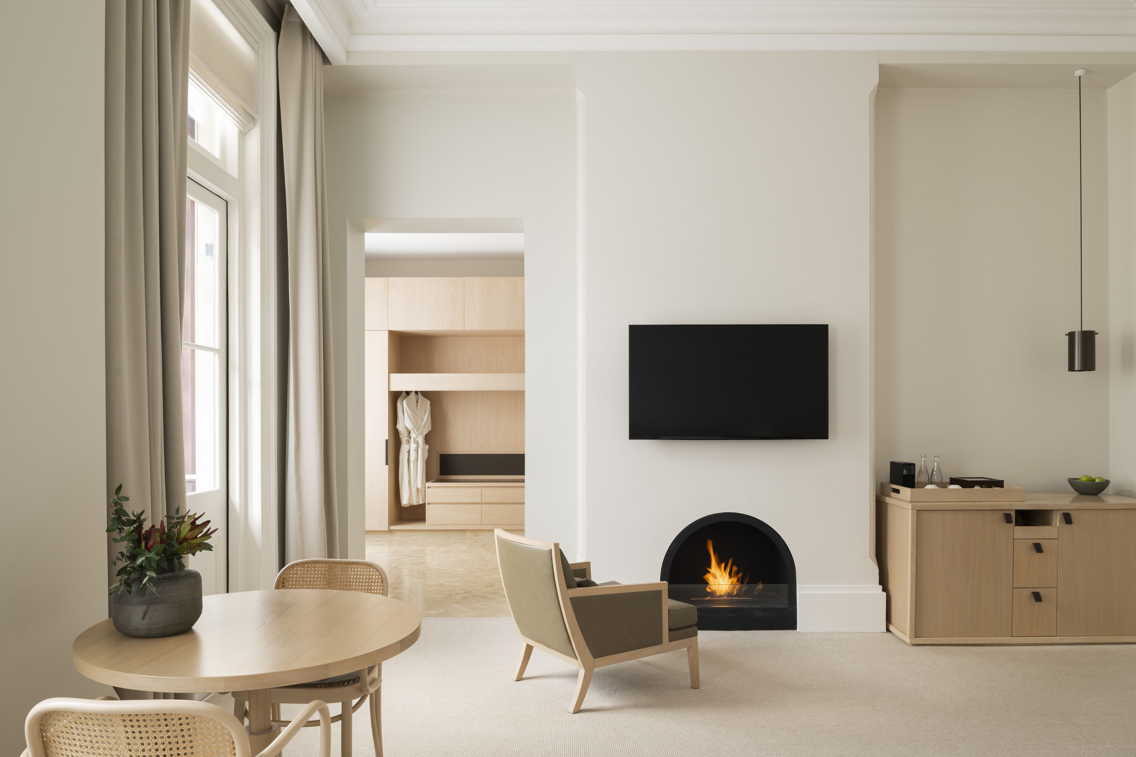 Una sala de estar moderna con chimenea, un televisor de pantalla plana montado en la pared y un comedor con una mesa redonda y sillas.