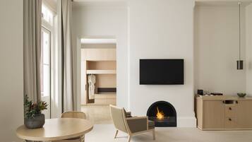 Una sala de estar moderna con chimenea, un televisor de pantalla plana montado en la pared y un comedor con una mesa redonda y sillas.