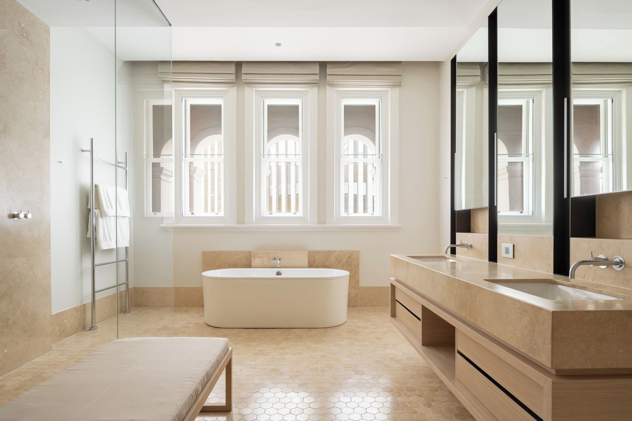 A modern bathroom with a freestanding bathtub, a large vanity with a mirror, and a window with a view of a building.