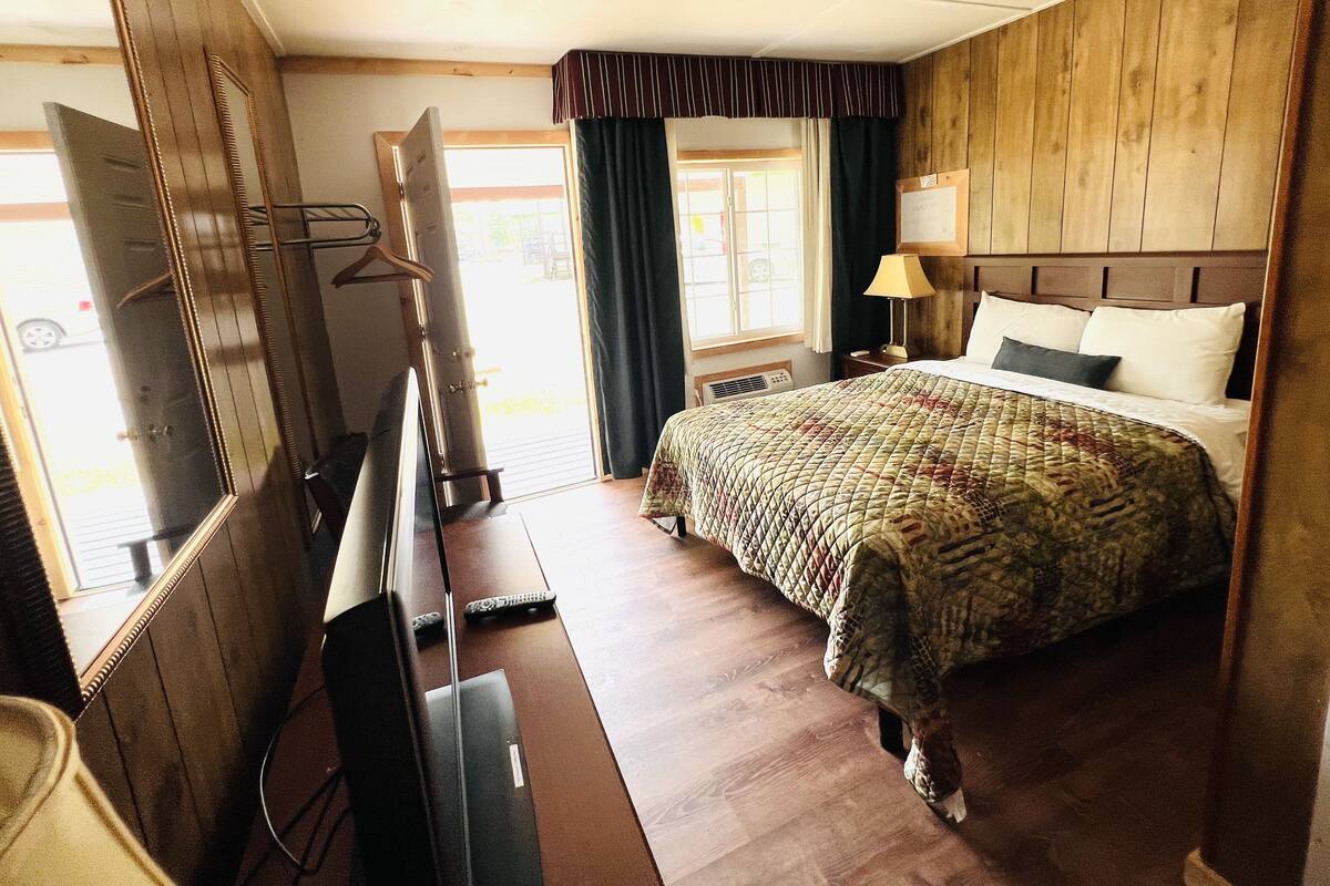 A bedroom with a bed, a TV, a desk, and a window with curtains.