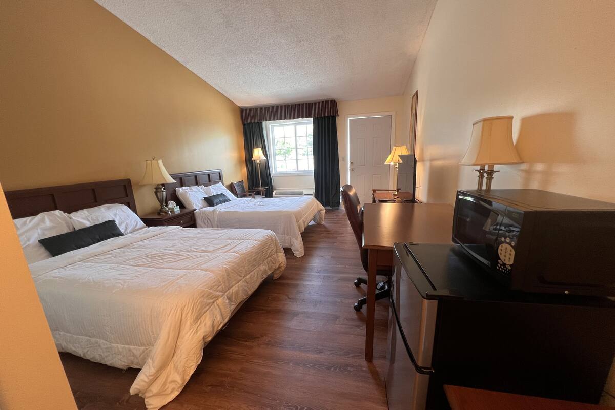 A hotel room with two beds, a desk, a chair, a TV, and a window with curtains.
