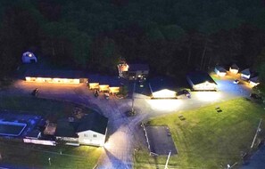 An aerial view of a residential area at night with multiple houses, a central building with lights, and a parking area.