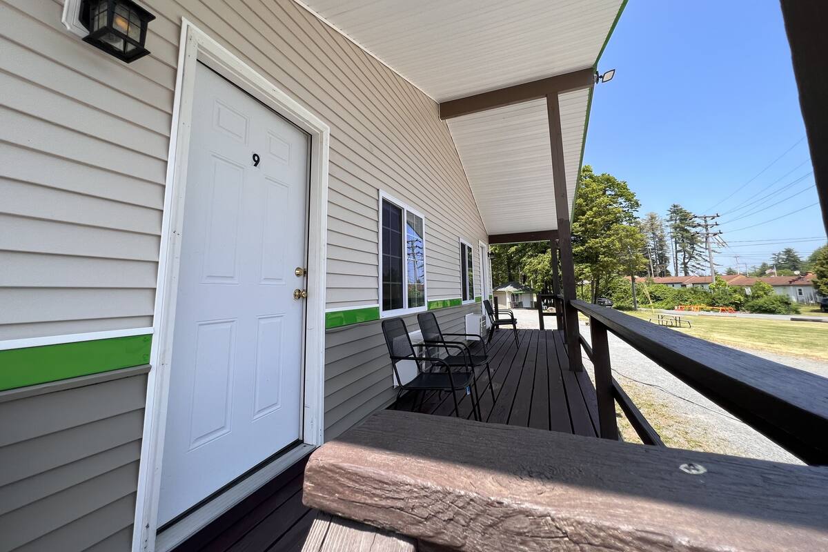 A covered porch with a white door marked with the number 9, a small outdoor seating area with chairs, and a view of a residential neighborhood.