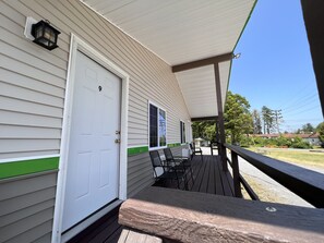 A covered porch with a white door marked with the number 9, a small outdoor seating area with chairs, and a view of a residential neighborhood.