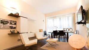 A modern living room with a sofa, ottoman, and a dining area with a table and chairs.