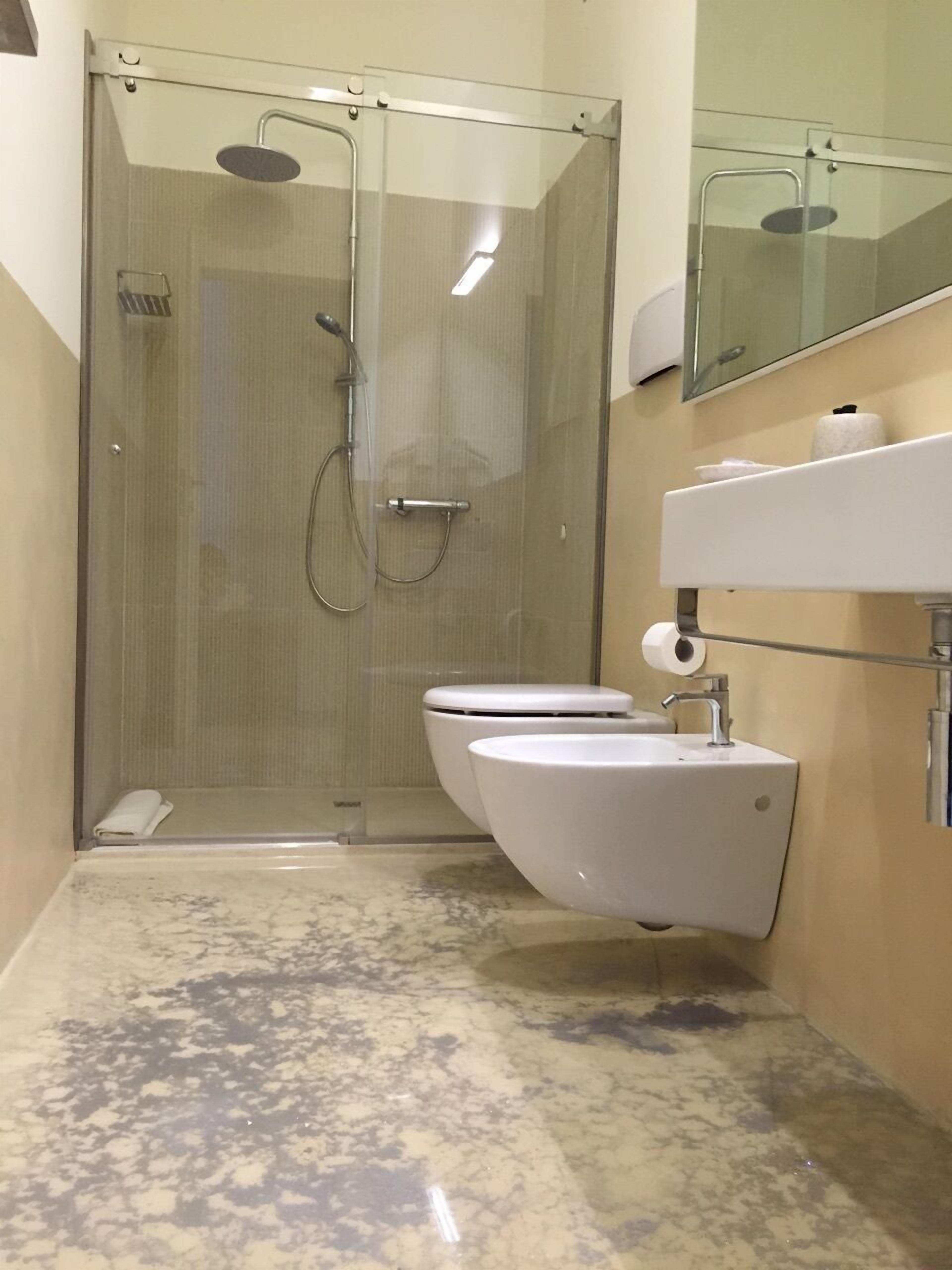 A bathroom with a glass-enclosed shower, two toilets, a sink, and a mirror.