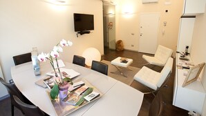 A modern meeting room with a white table, chairs, a TV, and a glass door leading to a hallway.