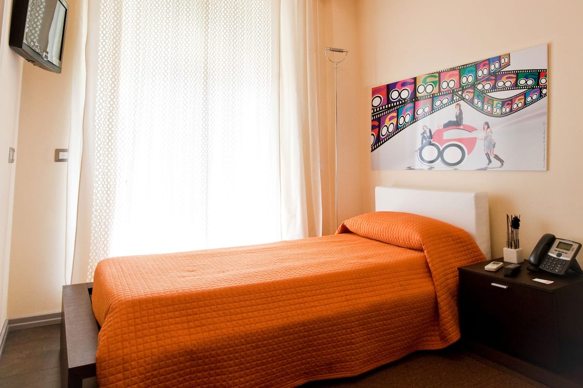 Hotelkamer met een bed, nachtkastje met telefoon, een wandtelevisie en raam met gordijnen.