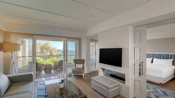 Ein modernes Hotelzimmer mit Balkon, Flachbildfernseher, Sofa, Esstisch und Bett.