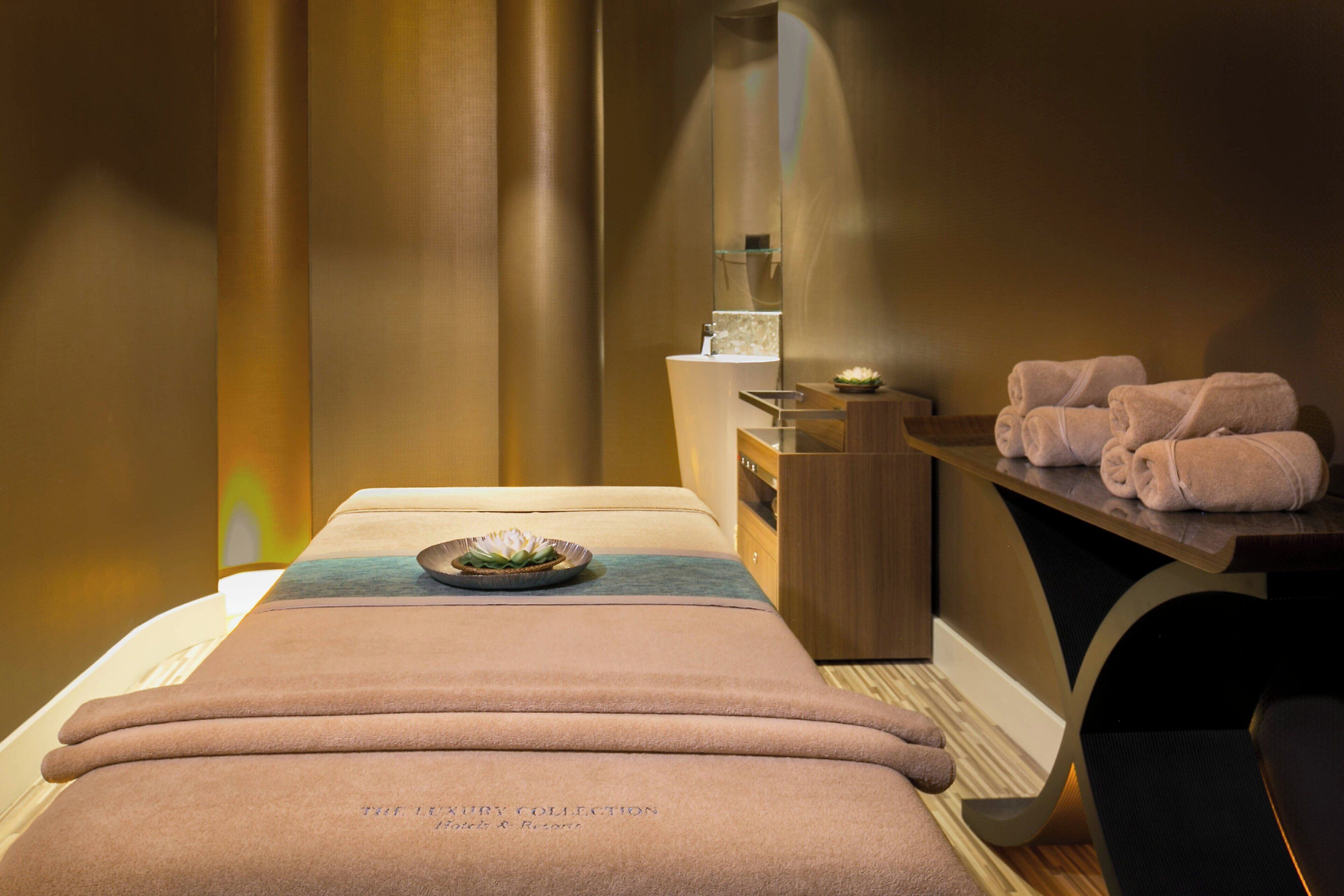 A spa room with a massage table, towels, a small shelf with a bowl, and a mirror.