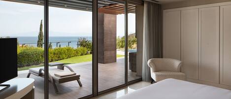 A modern hotel room with a large bed, a TV, and a view of a balcony with outdoor furniture.
