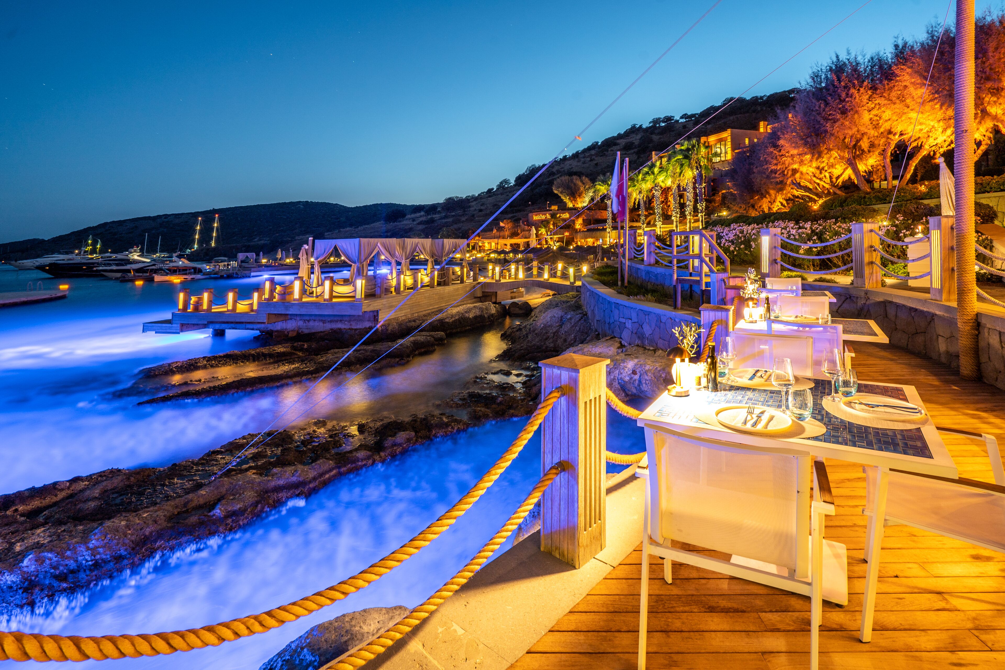 Un restaurant en bord de mer avec une terrasse offrant une vue sur l’océan, doté d’une plateforme en bois et donnant sur la côte.