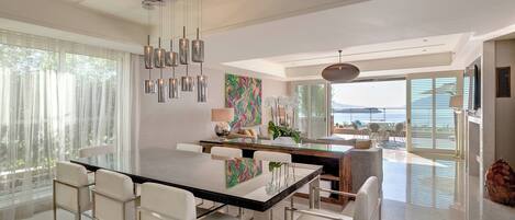 A modern dining area with a glass table, white chairs, and a view of the ocean.