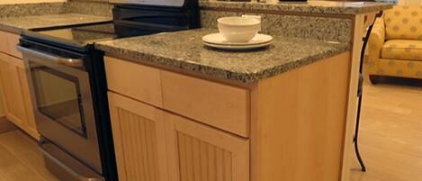 A kitchen with granite countertops, a built-in oven, wooden cabinets, and a small island with a bowl.