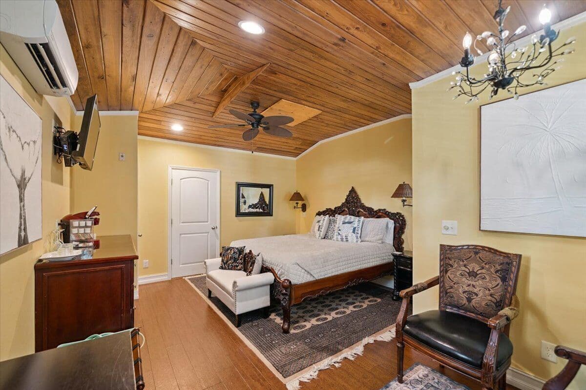 Quarto com teto de madeira, uma cama, uma cadeira, uma escrivaninha e um candelabro.