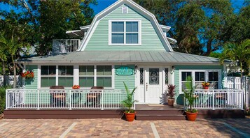 Un Seaglass Inn con fachada verde, detalles blancos y un pequeño porche con plantas en macetas.