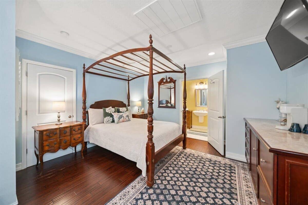 Quarto com cama de dossel, mesa de cabeceira, cômoda e televisão.