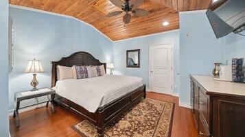 A bedroom with a wooden ceiling, a bed with a white quilt, two bedside lamps, a patterned rug, and a wooden cabinet.