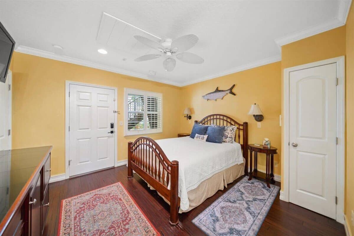 Quarto com cama de madeira, ventoinha no teto, decoração de parede com peixes e janela com persianas.