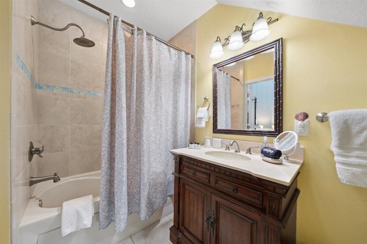 A bathroom with a bathtub, shower, vanity with a mirror, and a towel rack.