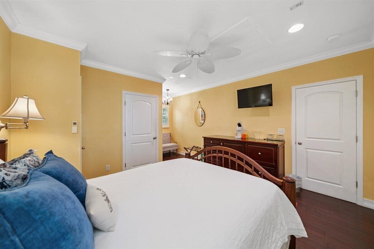 A bedroom with a bed, a dresser, a chair, a ceiling fan, and a television on the wall.