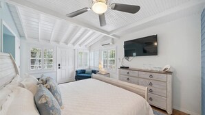 Une chambre à coucher avec un grand lit, un ventilateur de plafond, un téléviseur fixé au mur et une commode.