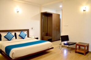 A bedroom with a bed, a chair, a small table, and a wardrobe. - Hotel Marc Inn (Jaipur)