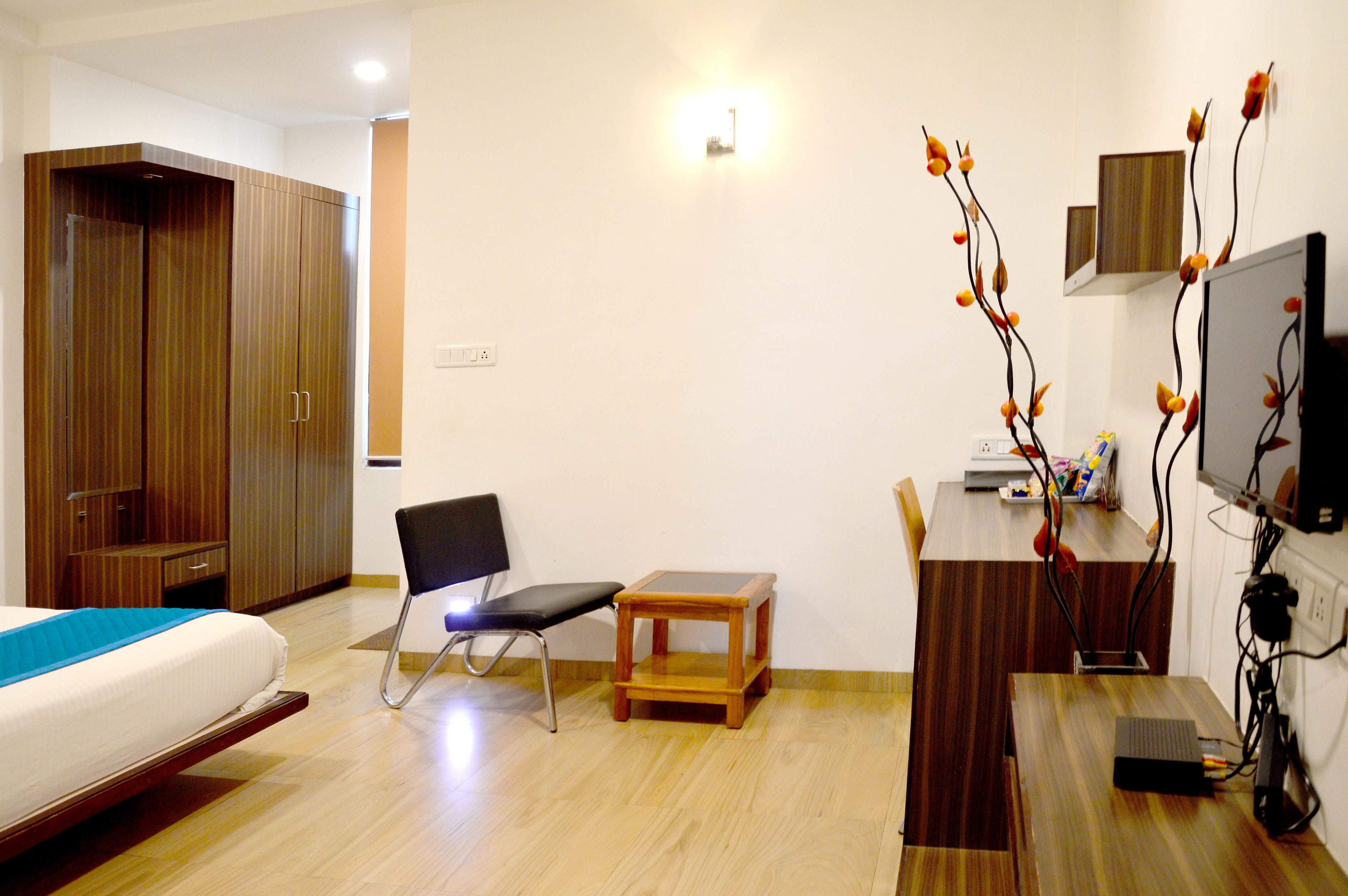 A hotel room with a bed, a desk, a chair, a small table, a wardrobe, and a TV.