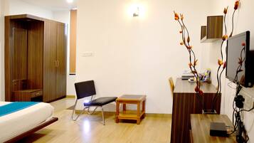 A hotel room with a bed, a desk, a chair, a small table, a wardrobe, and a TV.