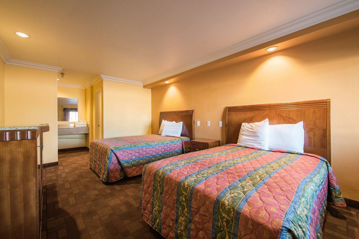 Ein Hotelzimmer mit zwei Betten, Holz-Kopfteilen und einem kleinen Schreibtisch mit Spiegel.