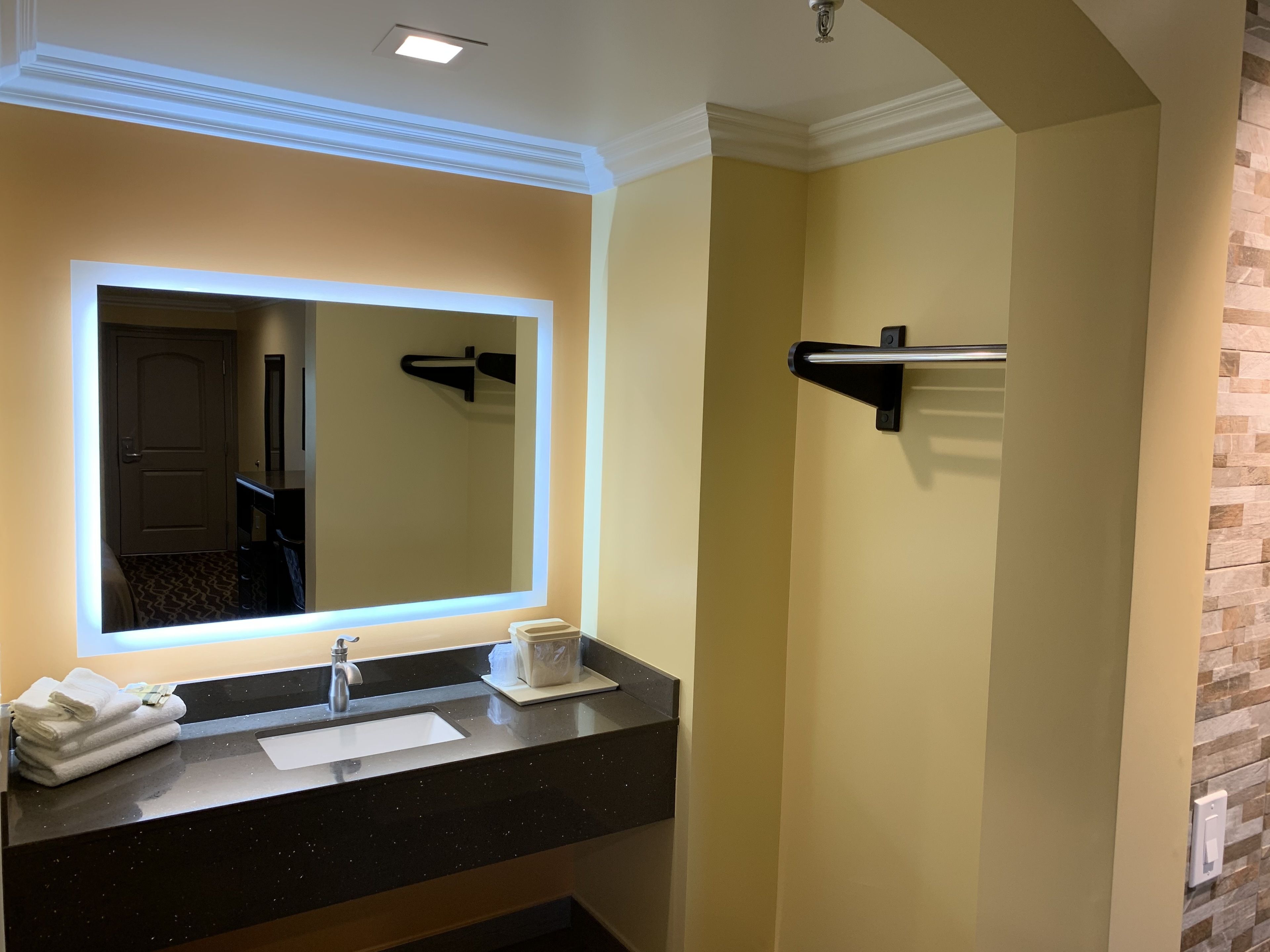 A bathroom with a large mirror, a sink, and a towel rack.