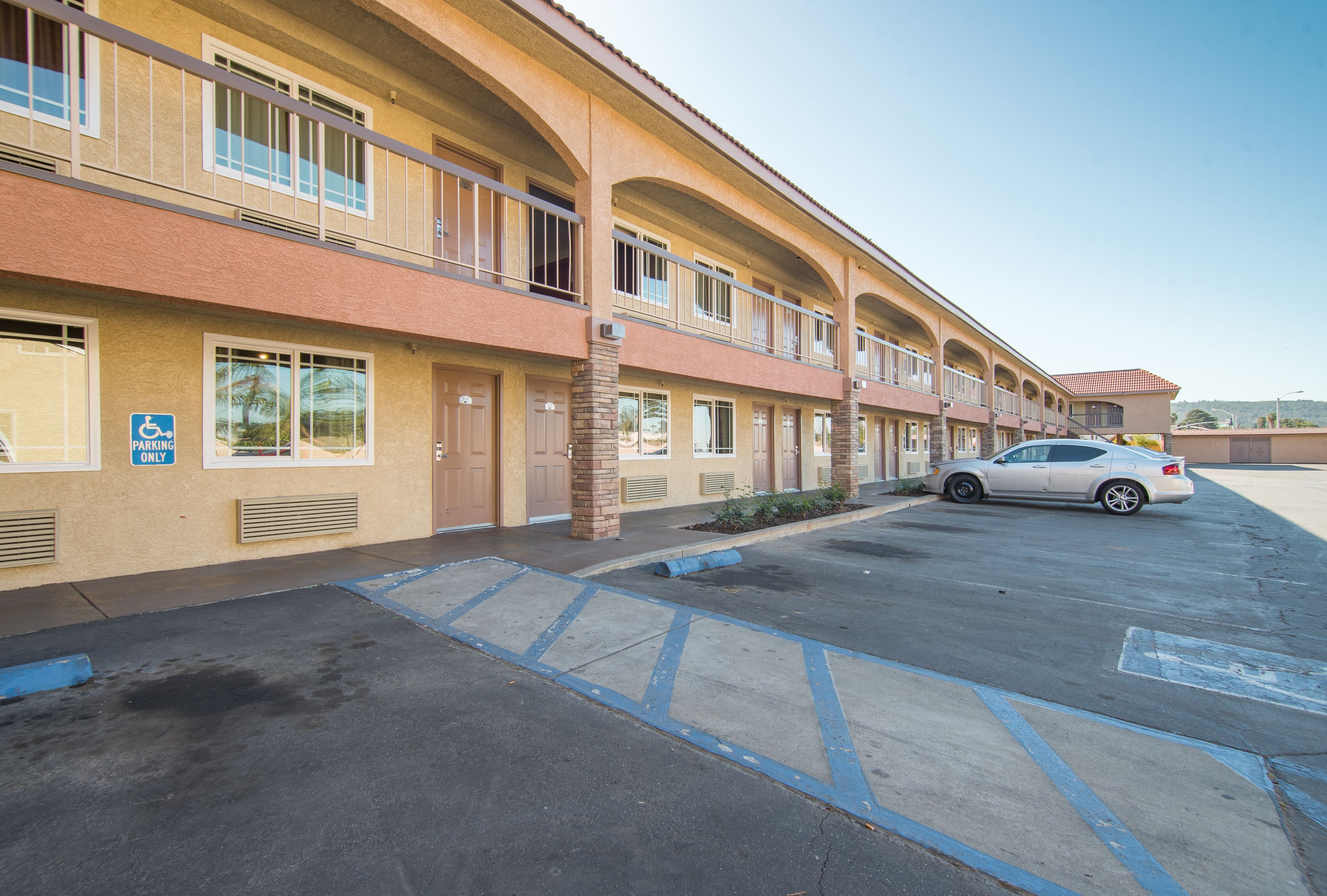 A multi-story motel with a parking lot, a handicapped parking sign, and a car parked in the lot.