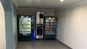 A clean, modern room with grey tiled floors, a central ice dispenser, and vending machines on either side. - Industry Inn & Suites (La Puente)