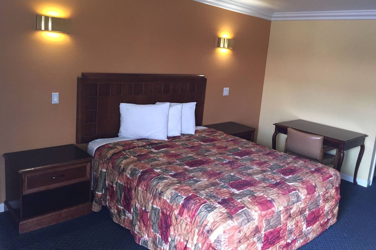 Ein Hotelzimmer mit einem großen Bett, zwei Nachttischen, einem Schreibtisch mit Stuhl und zwei Wandleuchten.