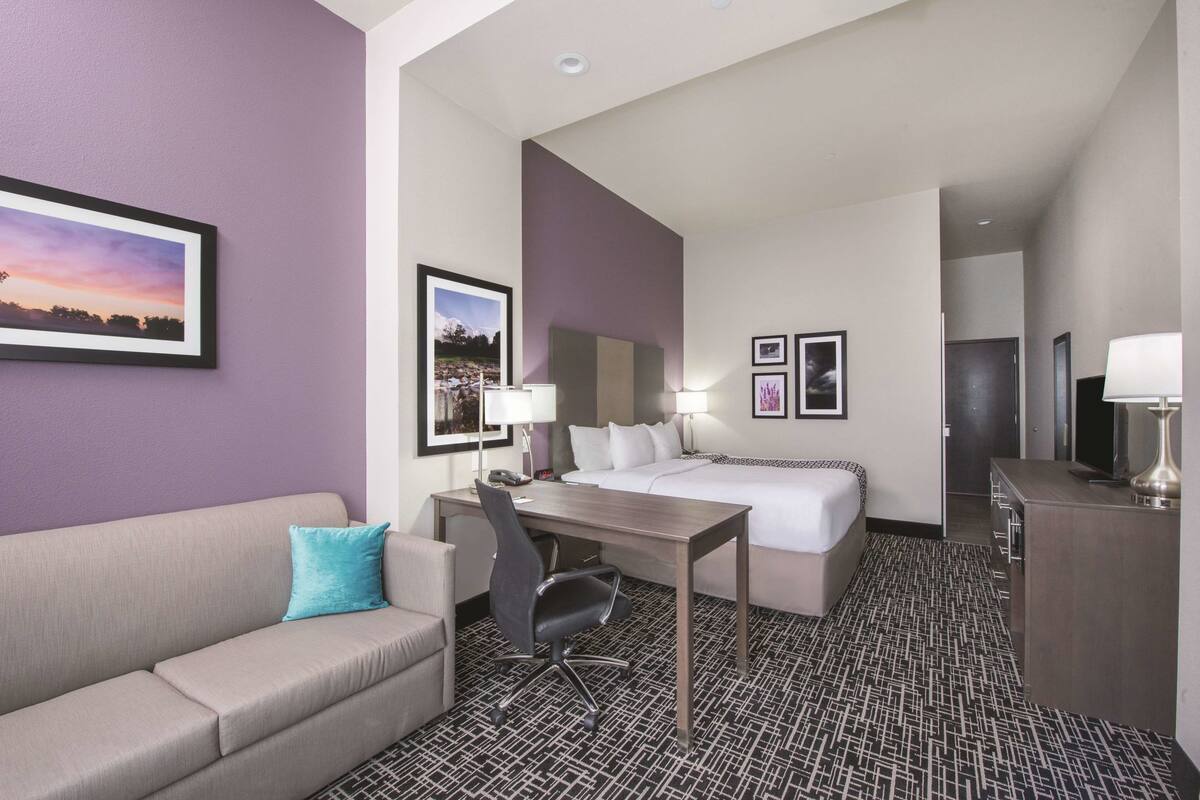 A hotel room with a bed, a desk, a chair, a sofa, and a TV.