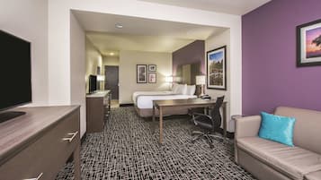 Habitación de hotel con cama, escritorio, silla, televisor y sofá con almohada.