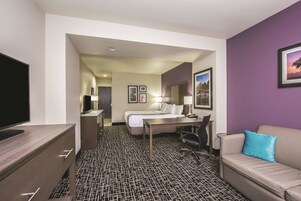 Habitación de hotel con cama, escritorio, silla, televisor y sofá con almohada.