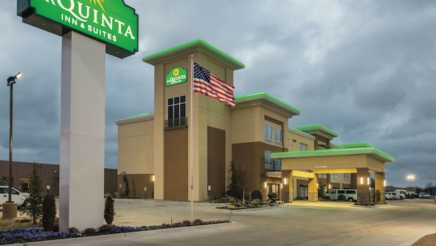 A La Quinta Inn & Suites building with a large sign, an American flag, and a parking lot. - La Quinta Inn & Suites by Wyndham Enid (Enid)