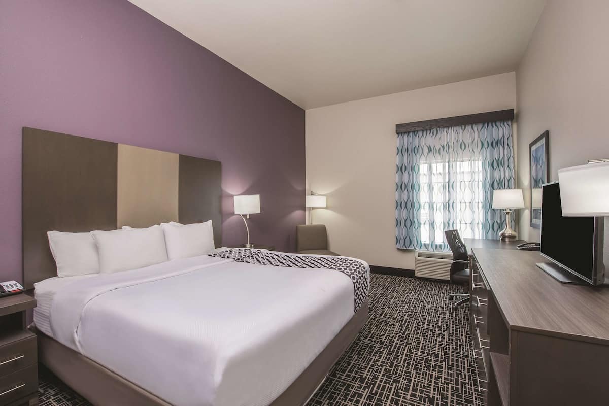 A hotel room with a large bed, two bedside tables, a desk with a chair, and a television.