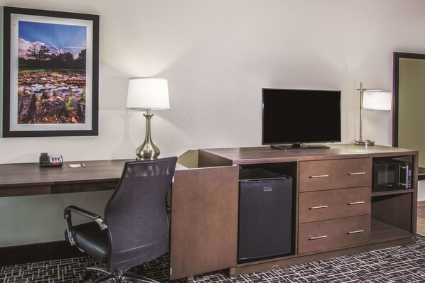 Habitación de hotel con escritorio, silla, televisión, mini refrigerador, microondas y un cuadro en la pared.