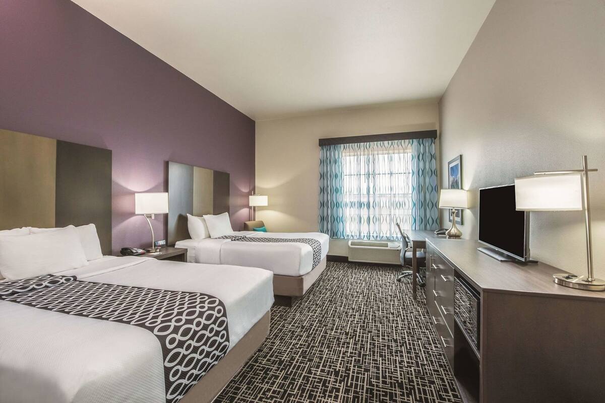 A hotel room with two beds, a desk with a TV, and a window with curtains.