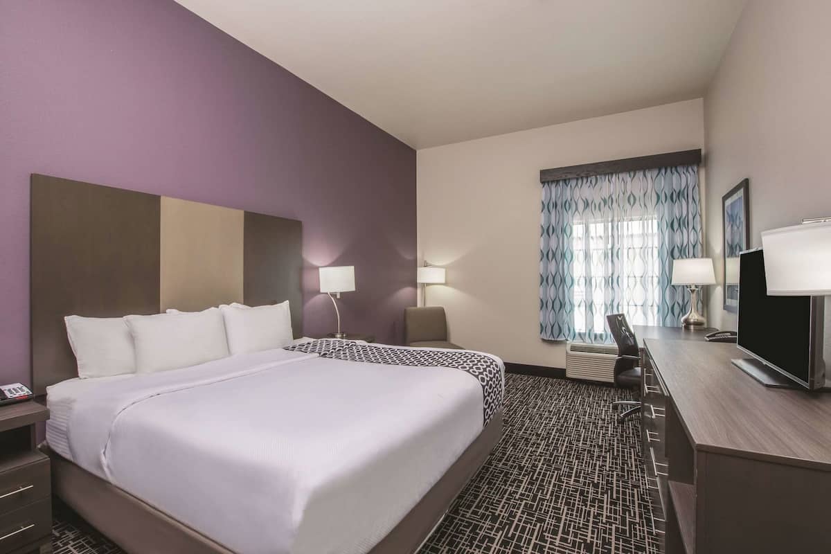 A hotel room with two beds, a desk, a chair, a TV, and a window with curtains.